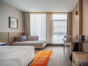 A hotel room with a bed, a sofa, a small table, and a window with curtains. - Novotel Zibo New Hongcheng (Zibo)