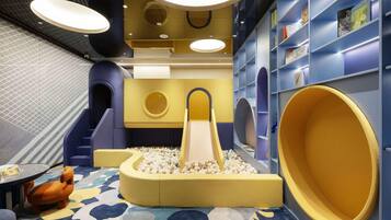 A children's play area with a ball pit, slides, and bookshelves.