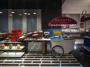 A Novotel hotel interior with a food display, seating area, and a sign indicating the hotel's name. - Novotel Zibo New Hongcheng (Zibo)