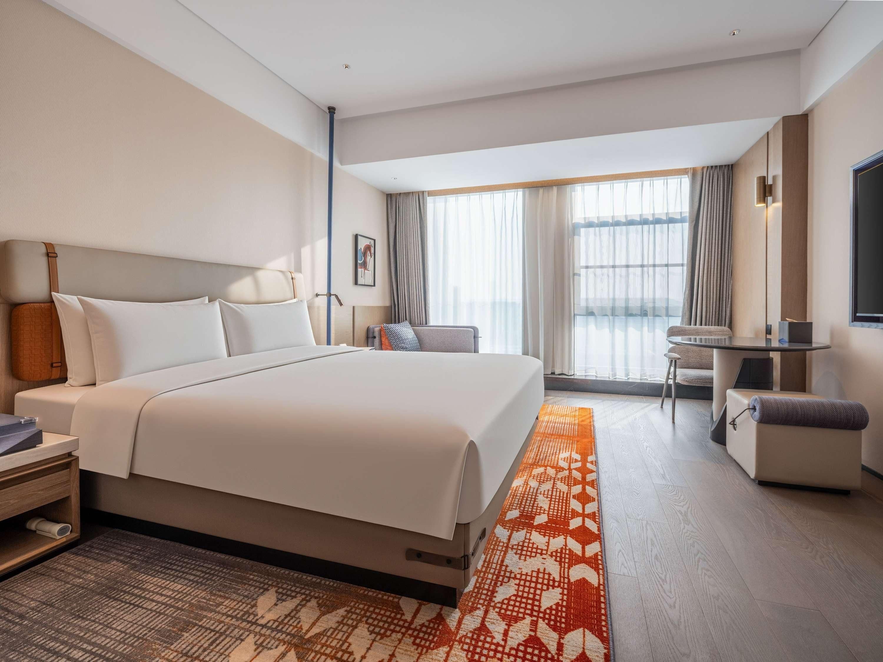 A modern hotel room with a large bed, a desk, and a chair.