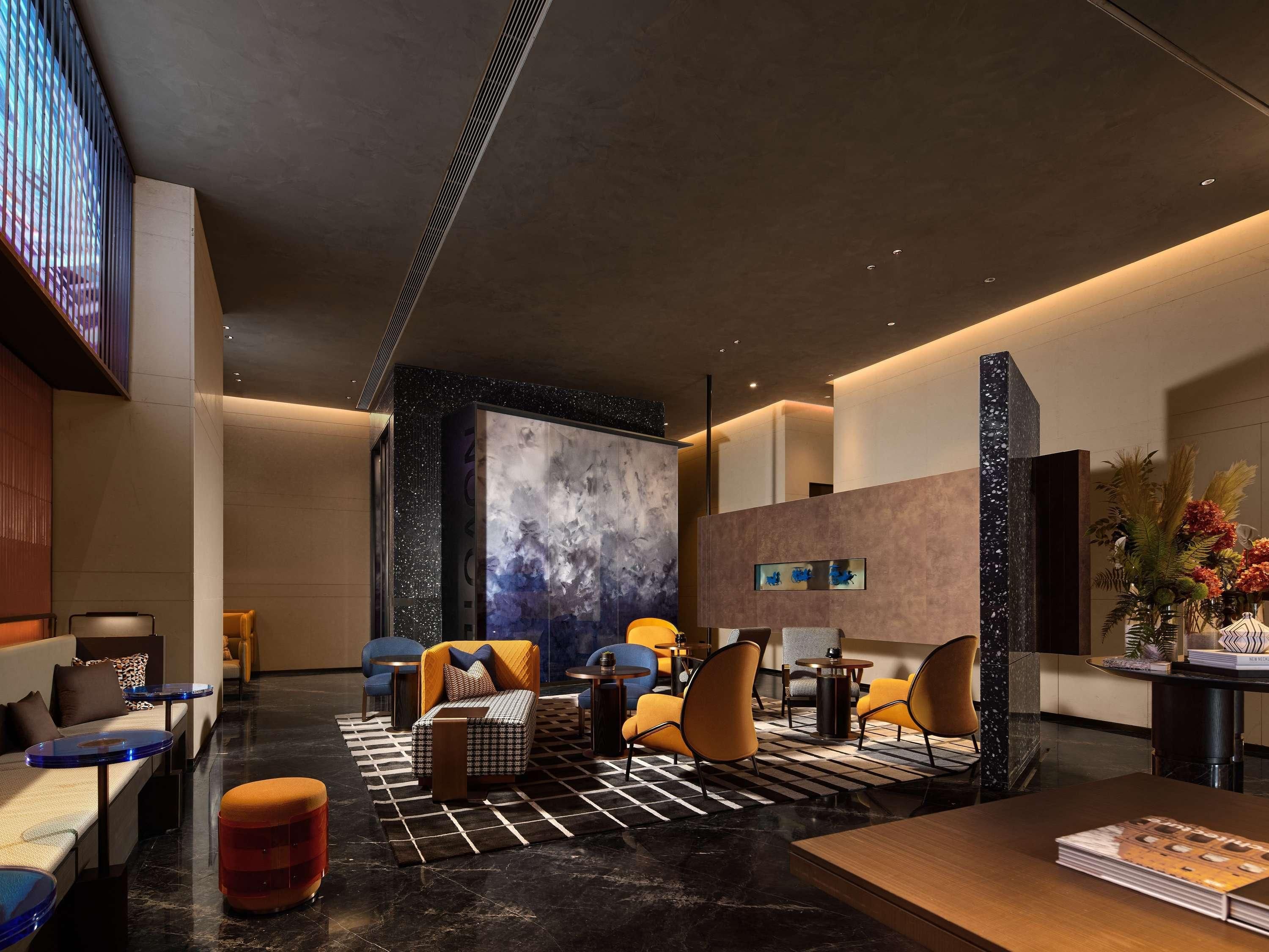 A modern lobby with a marble floor, seating areas, a large abstract wall art piece, and a reception desk with a vase of flowers.