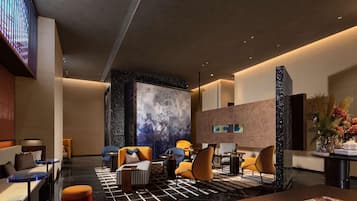 A modern lobby with a marble floor, seating areas, a large abstract wall art piece, and a reception desk with a vase of flowers.