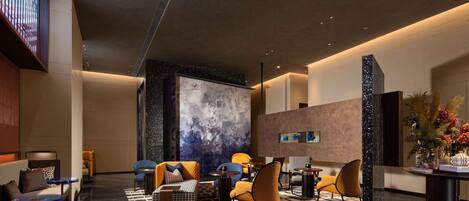 A modern lobby with a marble floor, seating areas, a large abstract wall art piece, and a reception desk with a vase of flowers.