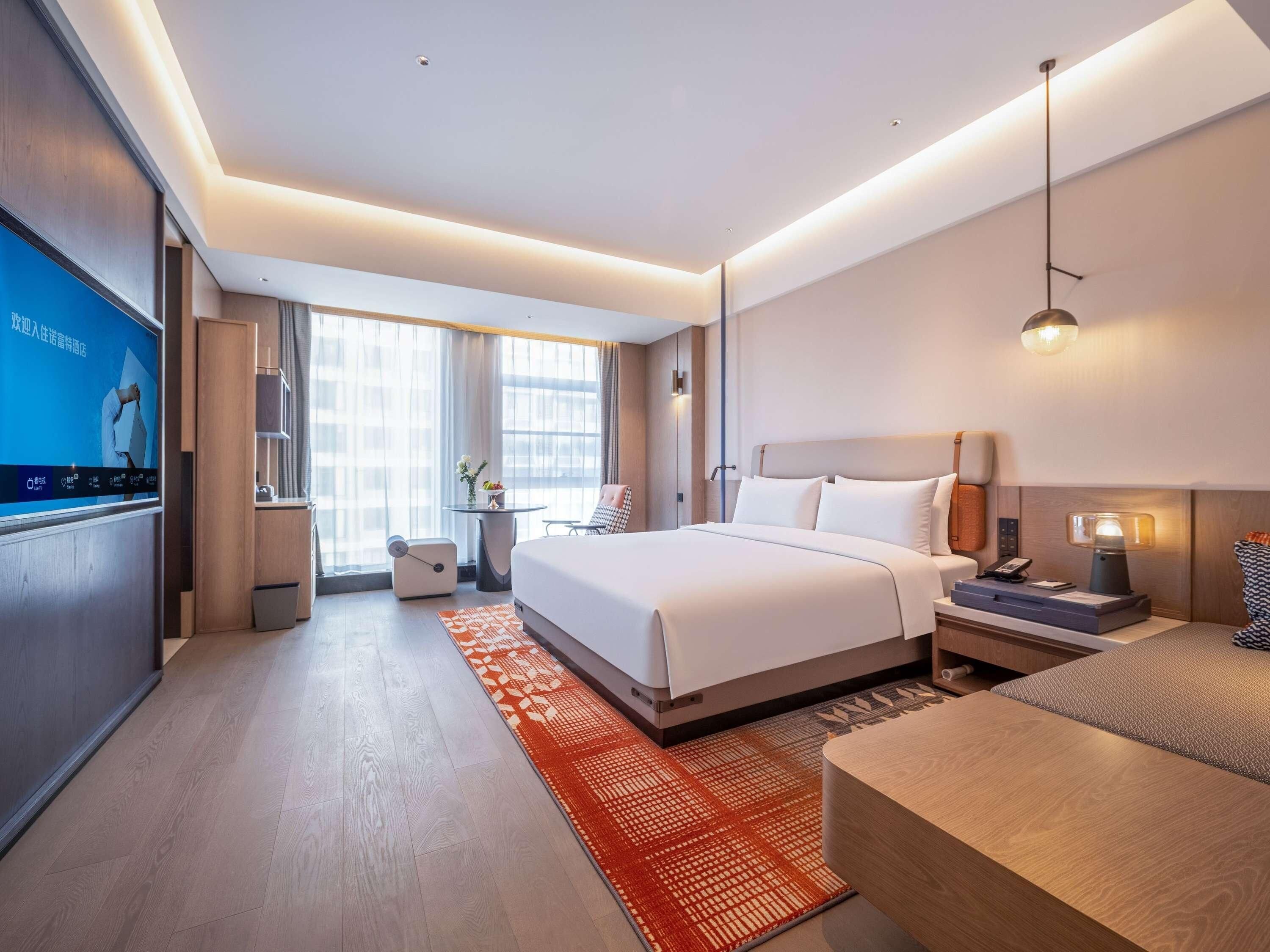 A modern hotel room with a large bed, bedside tables, a desk, and a TV.