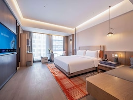 A modern hotel room with a large bed, bedside tables, a desk, and a TV.