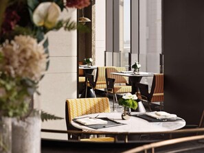 A restaurant with round tables and chairs, a vase with flowers, and a view through large windows. - Novotel Zibo New Hongcheng (Zibo)