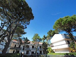 A residential building with multiple balconies, surrounded by trees and a clear blue sky. - Holiday apartment mit Terrasse und Pool (Lignano Sabbiadoro)