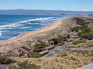 Zona residencial costeira com casas ao longo da praia, com vista clara para o oceano e colinas ao longe.