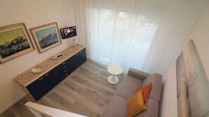 Una sala de estar moderna con un sofá, una mesa de centro y un televisor sobre un mueble. Hay dos cuadros enmarcados en la pared y una ventana con cortinas.