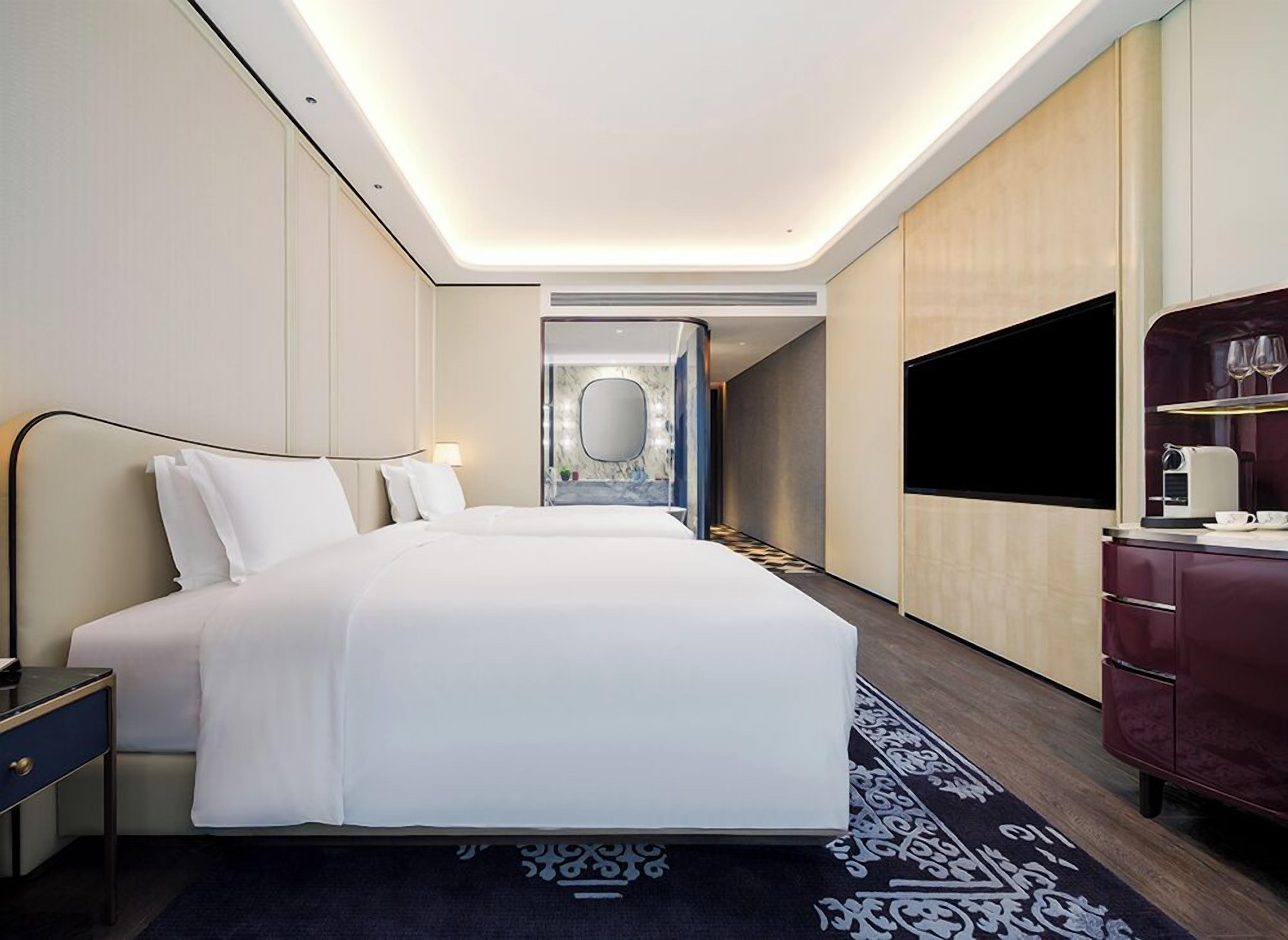 A modern hotel room with a large bed, bedside tables, a flat-screen TV, and a mirror.