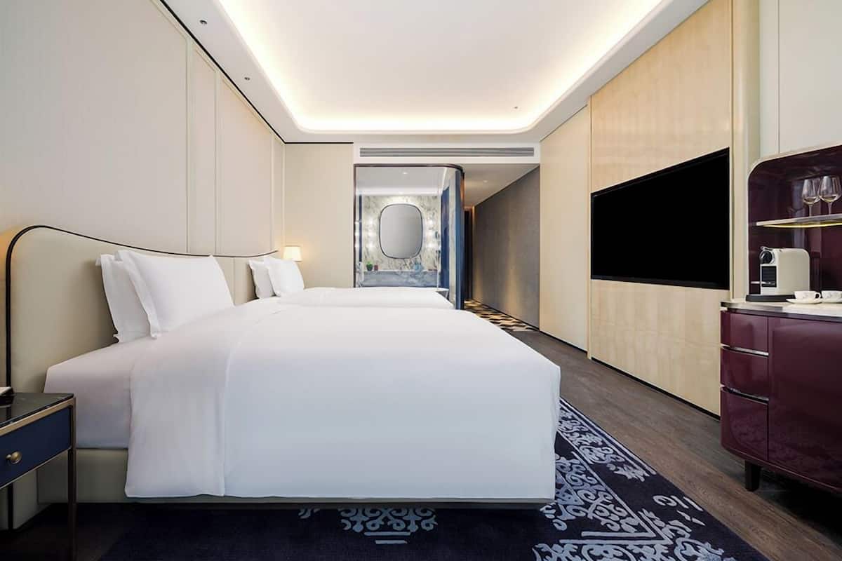 A modern hotel room with a large bed, bedside tables, a flat-screen TV, and a mirror.