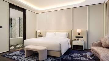 Une chambre d’hôtel moderne avec un grand lit, des tables de chevet avec des lampes, un petit tabouret et un tapis à motifs.