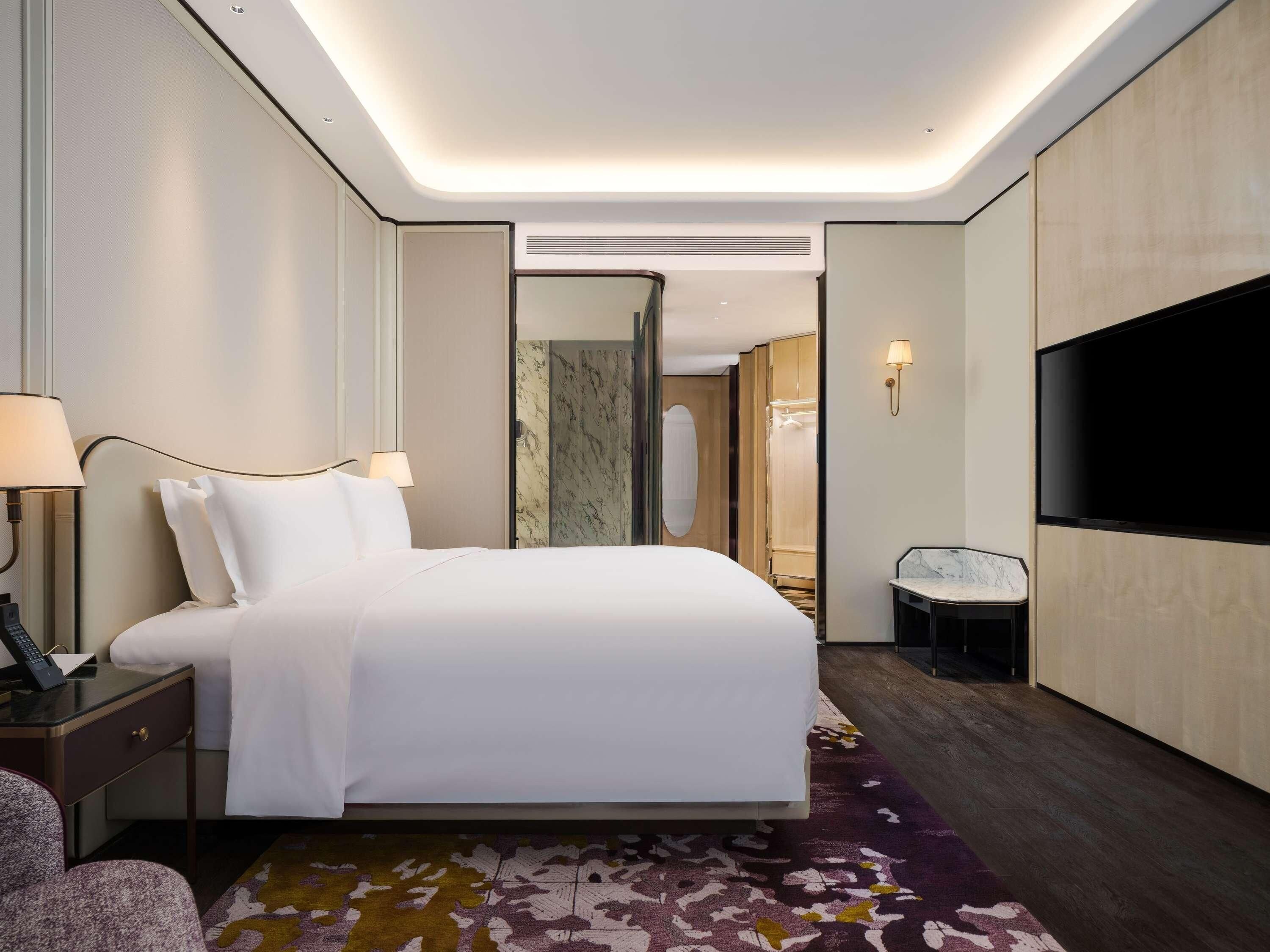 Una habitación de hotel con cama, mesitas de noche, televisor y zona de ducha.