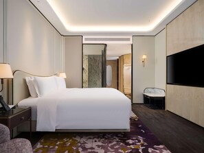 Una habitación de hotel con cama, mesitas de noche, televisor y zona de ducha.