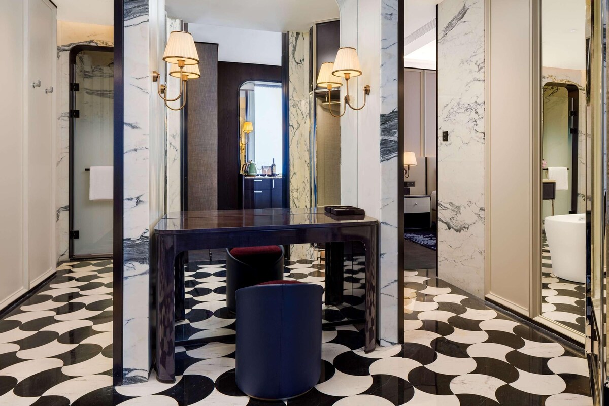 A modern bathroom with a marble floor, a glass-enclosed shower, and a vanity with a mirror and two wall-mounted lamps.