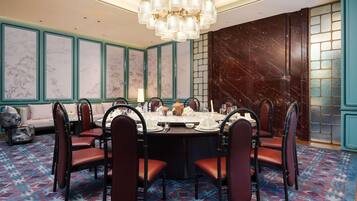 Comedor con una mesa redonda dispuesta para seis personas, rodeada de sillas tapizadas, en una habitación con alfombra estampada y paneles decorativos.