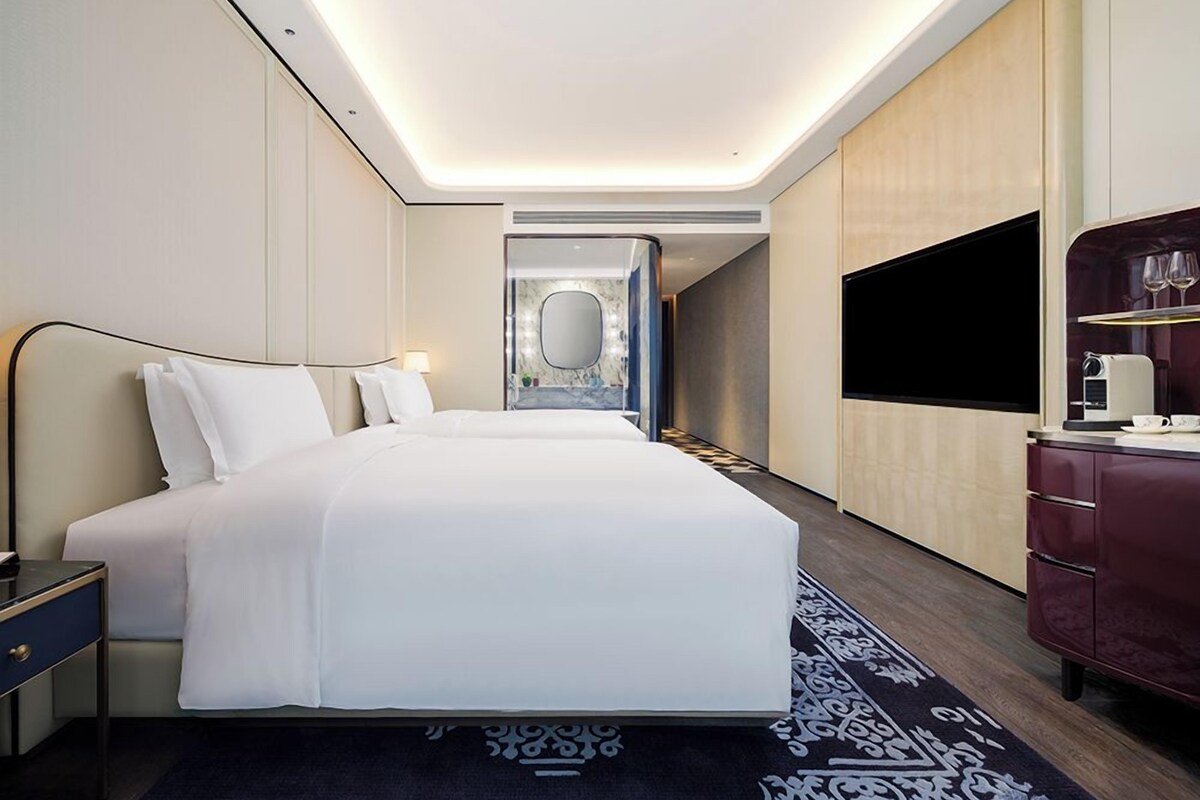A modern hotel room with a large bed, bedside tables, a flat-screen TV, and a mirror.