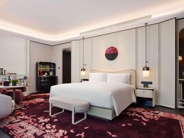 A modern hotel room with a large bed, bedside tables, a desk, and a wardrobe.
