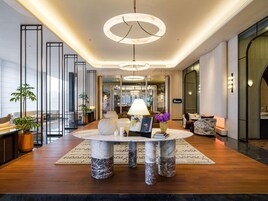 A modern hotel lobby with a marble table, seating, and a view of the city.