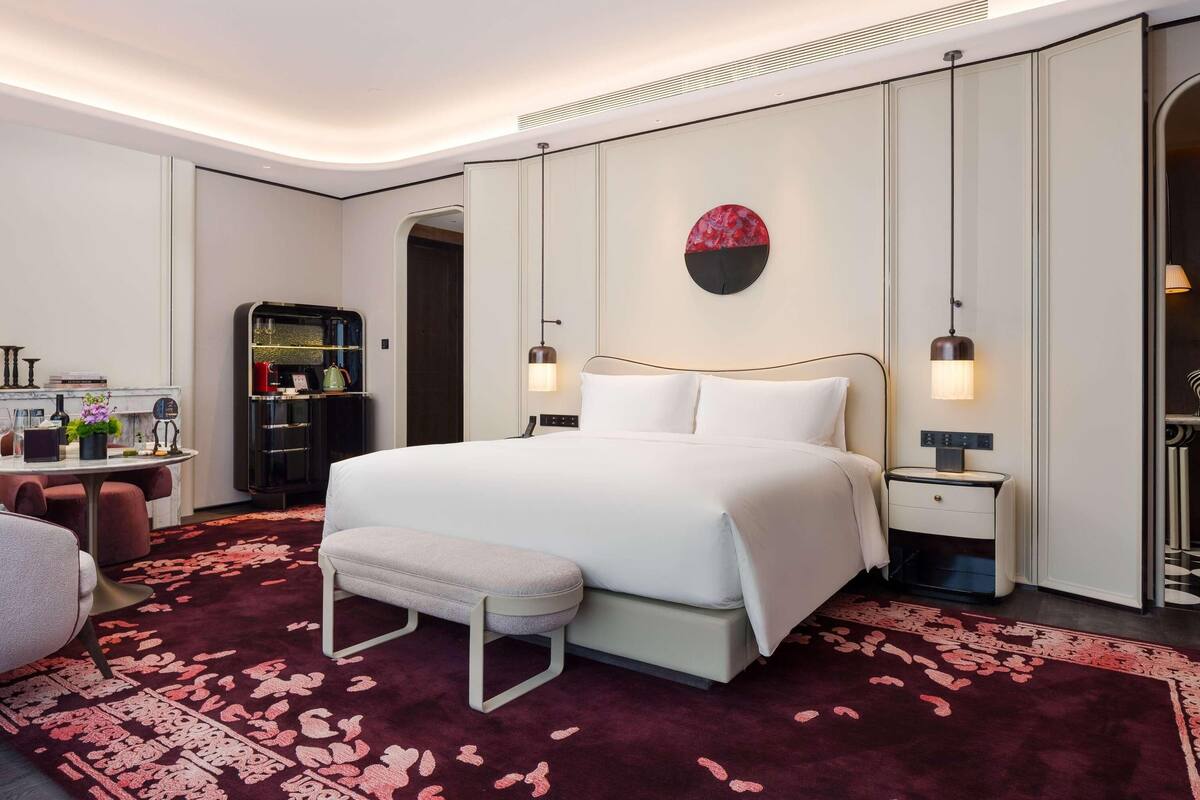 A modern hotel room with a large bed, bedside tables, a desk, and a wardrobe.