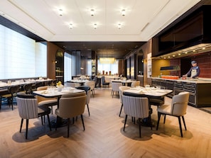 A modern restaurant with multiple dining tables, a bar area, and a chef preparing food. - Sofitel Changzhou Hi-tech District (Zhenjiang)
