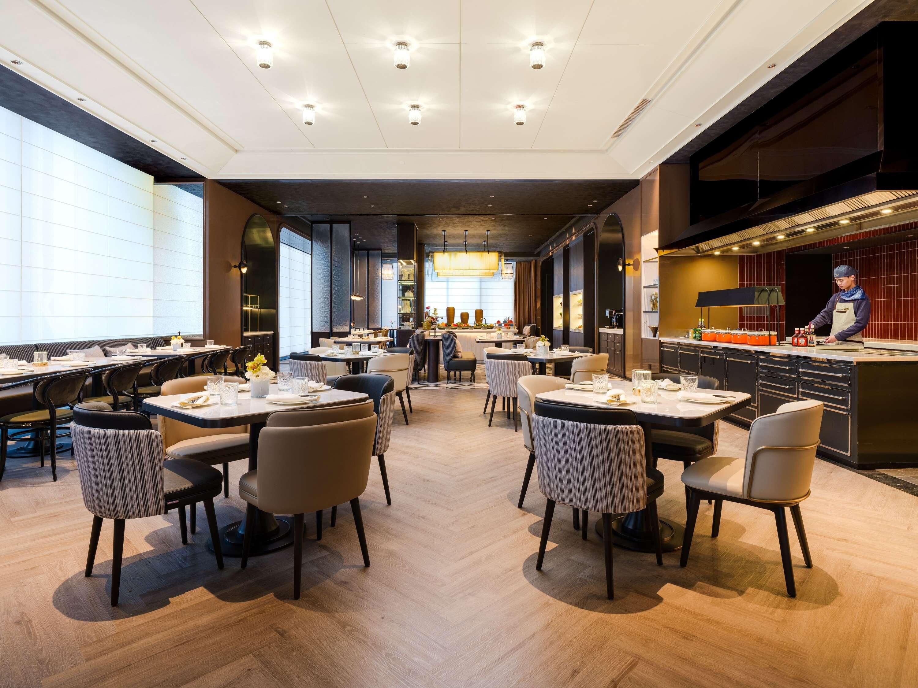 Un restaurante moderno con varias mesas, una zona de bar y un chef preparando comida.
