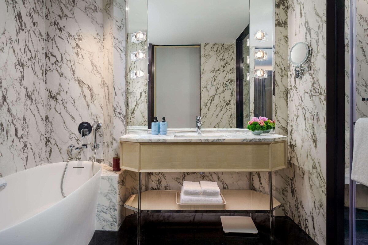 A bathroom with a marble wall, a bathtub, a vanity with a mirror, and a sink.