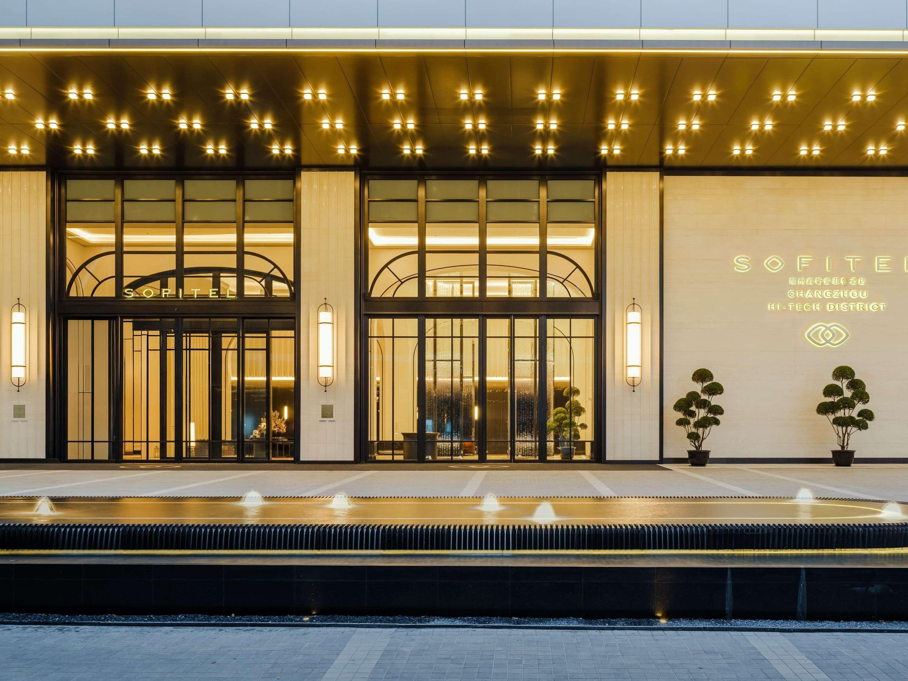 A modern hotel entrance with a water feature in front, large glass doors, and illuminated signage.