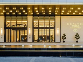 Una entrada de hotel moderna con una fuente, amplias puertas de vidrio y señalización iluminada.