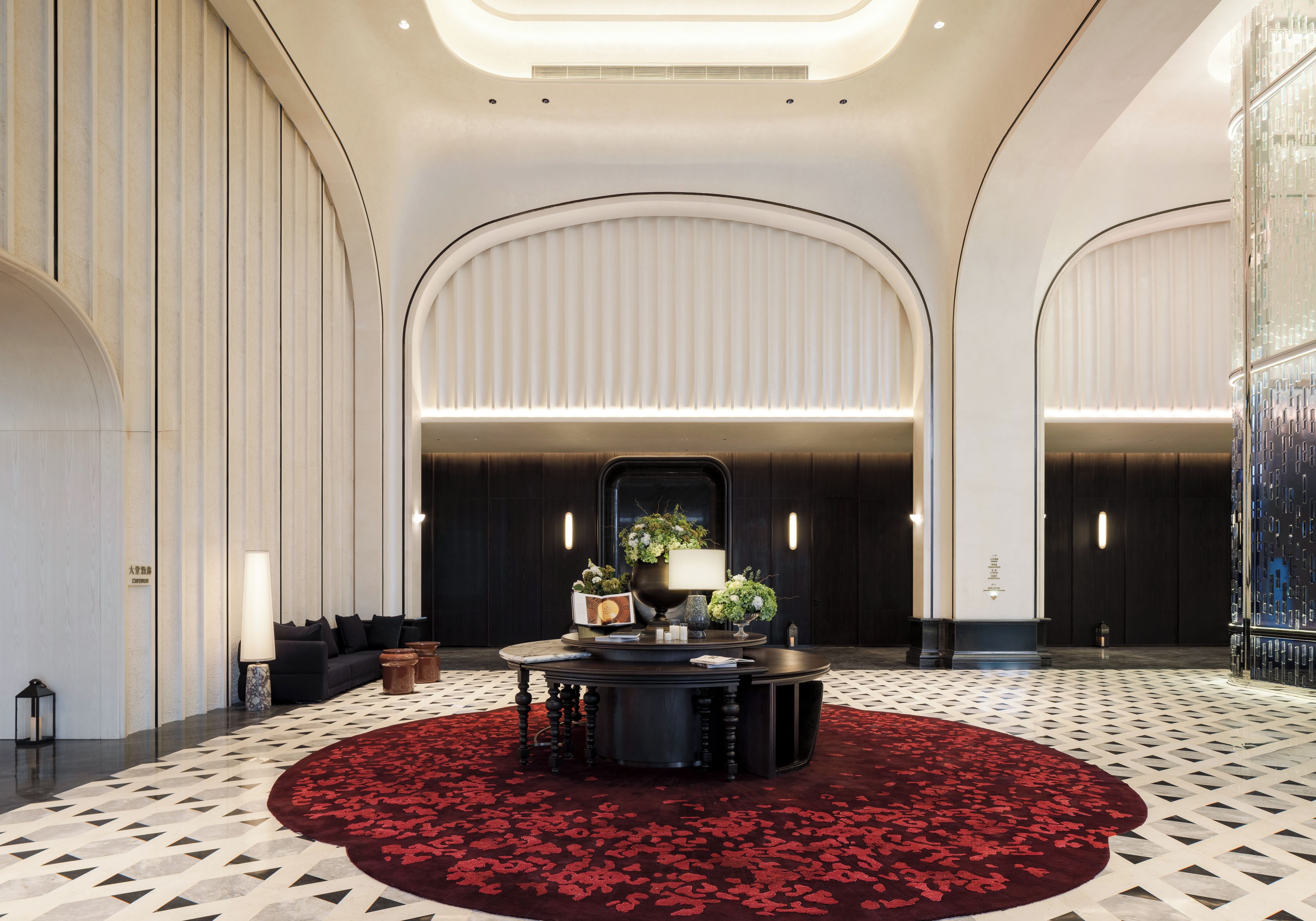 A lobby with a round table, a red carpet, and a large mirror.