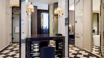 Un baño moderno con piso de mármol, ducha envuelta en vidrio y tocador con espejo y dos lámparas de pared.
