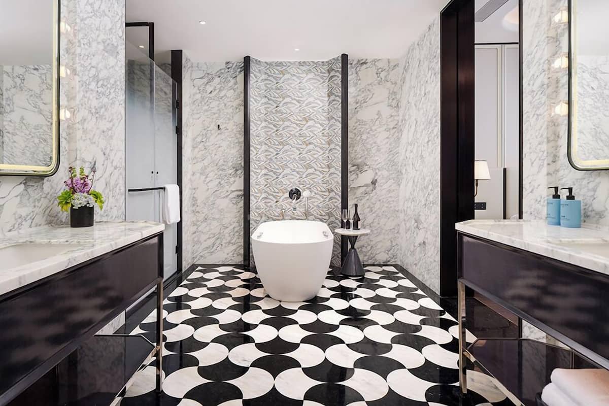 A modern bathroom with a freestanding bathtub, marble walls, and a black-and-white patterned floor.