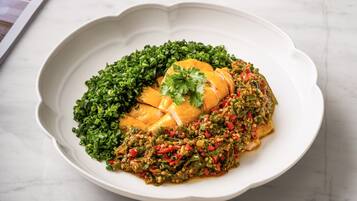 Un plato con un guiso de pollo, vegetales verdes y salsa, sobre un plato blanco.