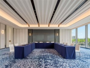 Ein Konferenzraum mit einem langen Tisch, weißen Stühlen und einem gemusterten Teppich.