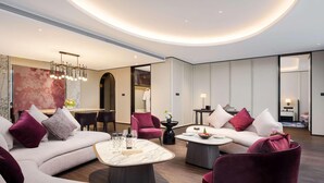 A modern hotel room with a living area featuring a sofa, armchairs, a coffee table, and a dining area with a table and chairs. - Sofitel Changzhou Hi-tech District (Zhenjiang)