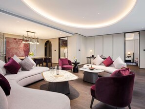 A modern hotel room with a living area featuring a sofa, armchairs, a coffee table, and a dining area with a table and chairs. - Sofitel Changzhou Hi-tech District (Zhenjiang)