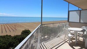 Ein Balkon mit Blick auf den Strand, einem Tisch mit Stühlen und einem Geländer.
