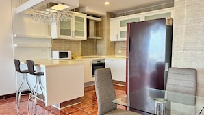 Una cocina compacta con microondas, una mesa de vidrio y dos taburetes de bar.