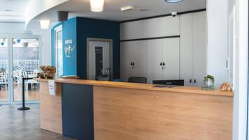 A hotel reception desk with a blue accent wall, a glass door entrance, and a security camera above the door.