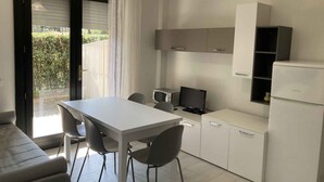 A modern kitchen with a dining area, featuring a white table, chairs, a built-in oven, and a refrigerator. - Holiday apartment mit Pool und Terrasse (Lignano Sabbiadoro)