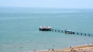 A pier extending into calm waters with a building at the end, a beach with umbrellas, and a clear sky. - Holiday apartment mit Balkon und Meerblick (Lignano Sabbiadoro)