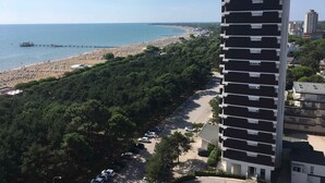 A high-rise building with a modern architectural design, adjacent to a beach with a pier. - Holiday apartment mit Balkon und Meerblick (Lignano Sabbiadoro)