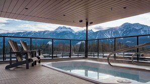 Een hottub met uitzicht op de bergen, een houten terras en Adirondack-stoelen.