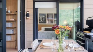 Een eettafel met een bloevas, borden, glazen, een grill en een bed op de achtergrond.
