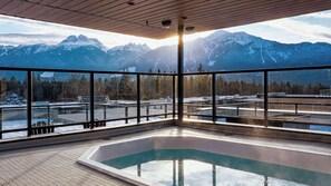Ein modernes Hallenbad mit Panoramablick auf schneebedeckte Berge und eine bewaldete Landschaft.