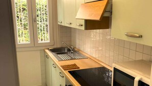 A compact kitchen with a sink, stove, microwave, and light green cabinets. - Holiday apartment mit Terrasse (Lignano Sabbiadoro)