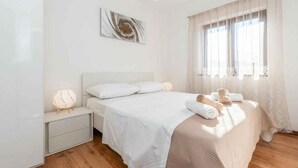 Ein Schlafzimmer mit Bett, Nachttischen, einem Wandbild und einem Fenster mit Vorhängen.