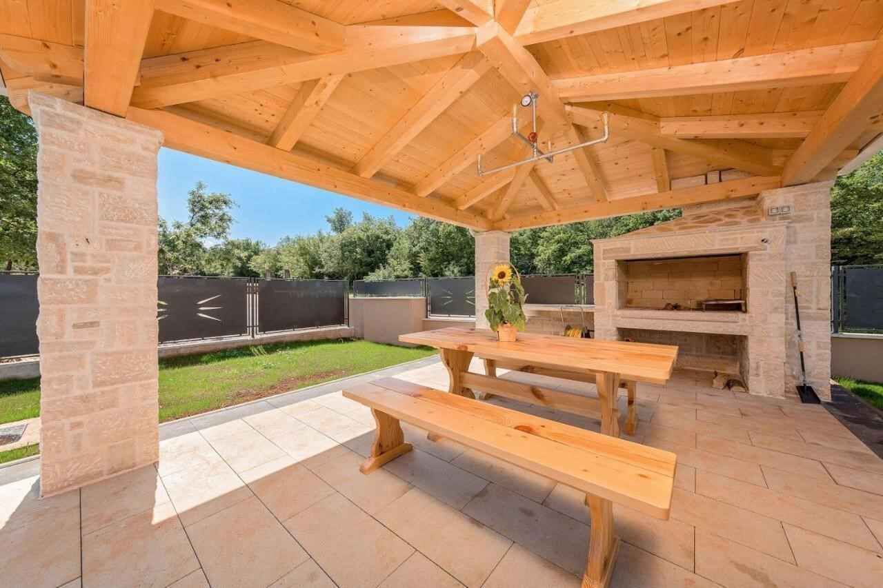 Una veranda esterna con panche di legno e un pilastro in pietra, un camino in pietra e una zona coperta con tetto in legno.