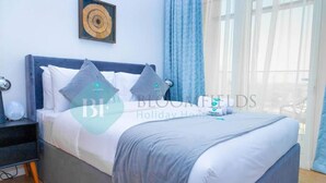 A neatly made bed with a grey bedspread and pillows, a bedside table with a lamp, and a wall-mounted artwork. - -Bloomfields Modern 1BR in Oasis Masd (Abu Dhabi)