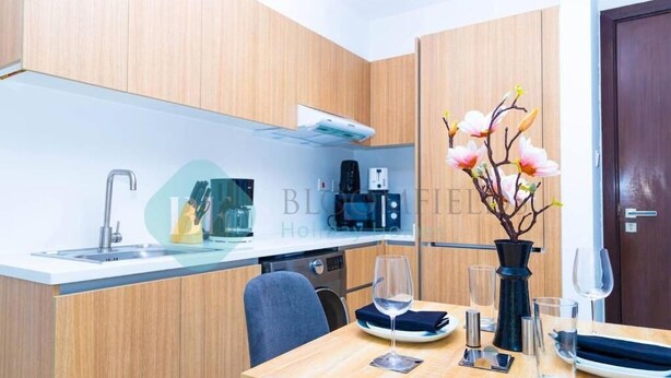 A modern kitchen with a built-in oven, a coffee machine, and a sink. There is a dining table with a vase of flowers and a wine glass. - -Bloomfields Modern 1BR in Oasis Masd (Abu Dhabi)